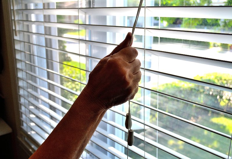 Hand adjusting white vinyl blinds on sunny window in Tucson, AZ